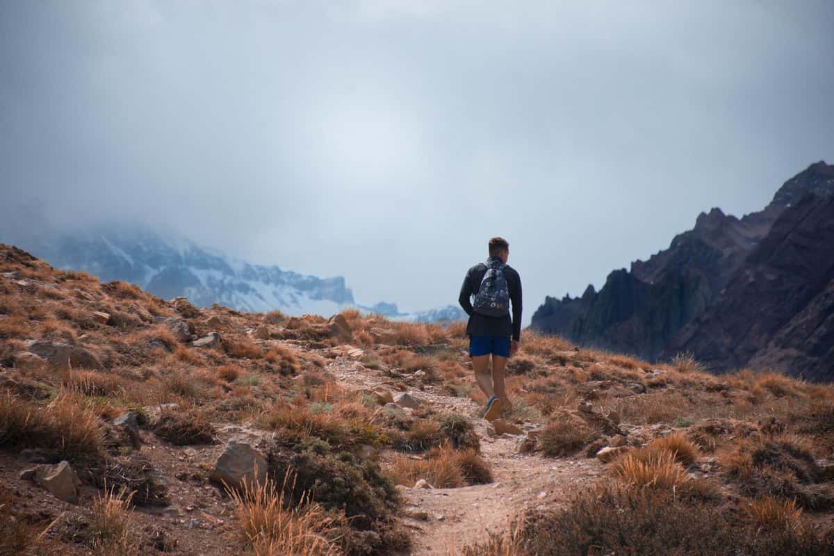 A man walking alone up a mountain path toward distant peaks